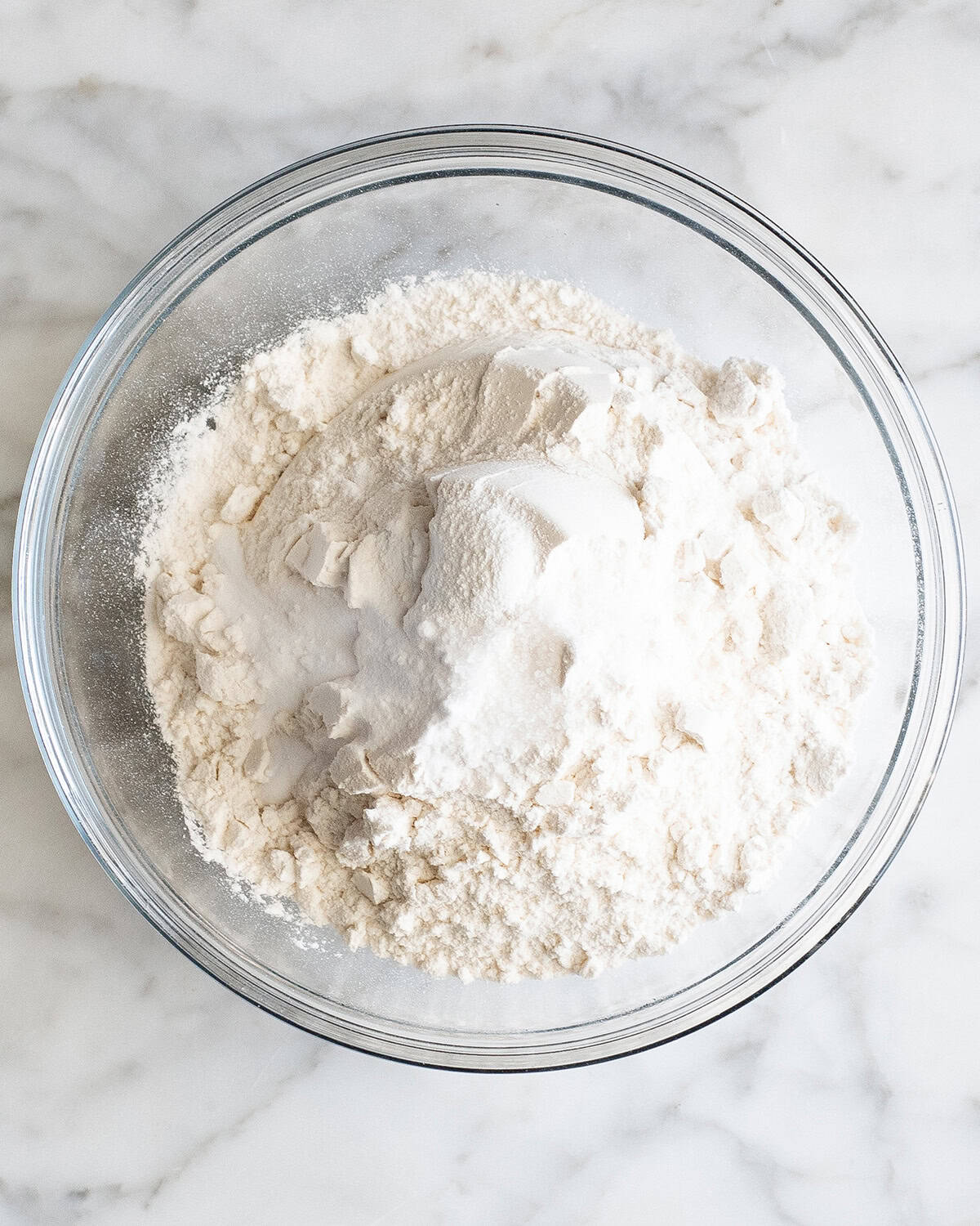how to make chocolate chip cookies - flour, baking soda, baking powder and salt in a glass bowl on a marble surface before mixing together making the best chocolate chip cookies recipe