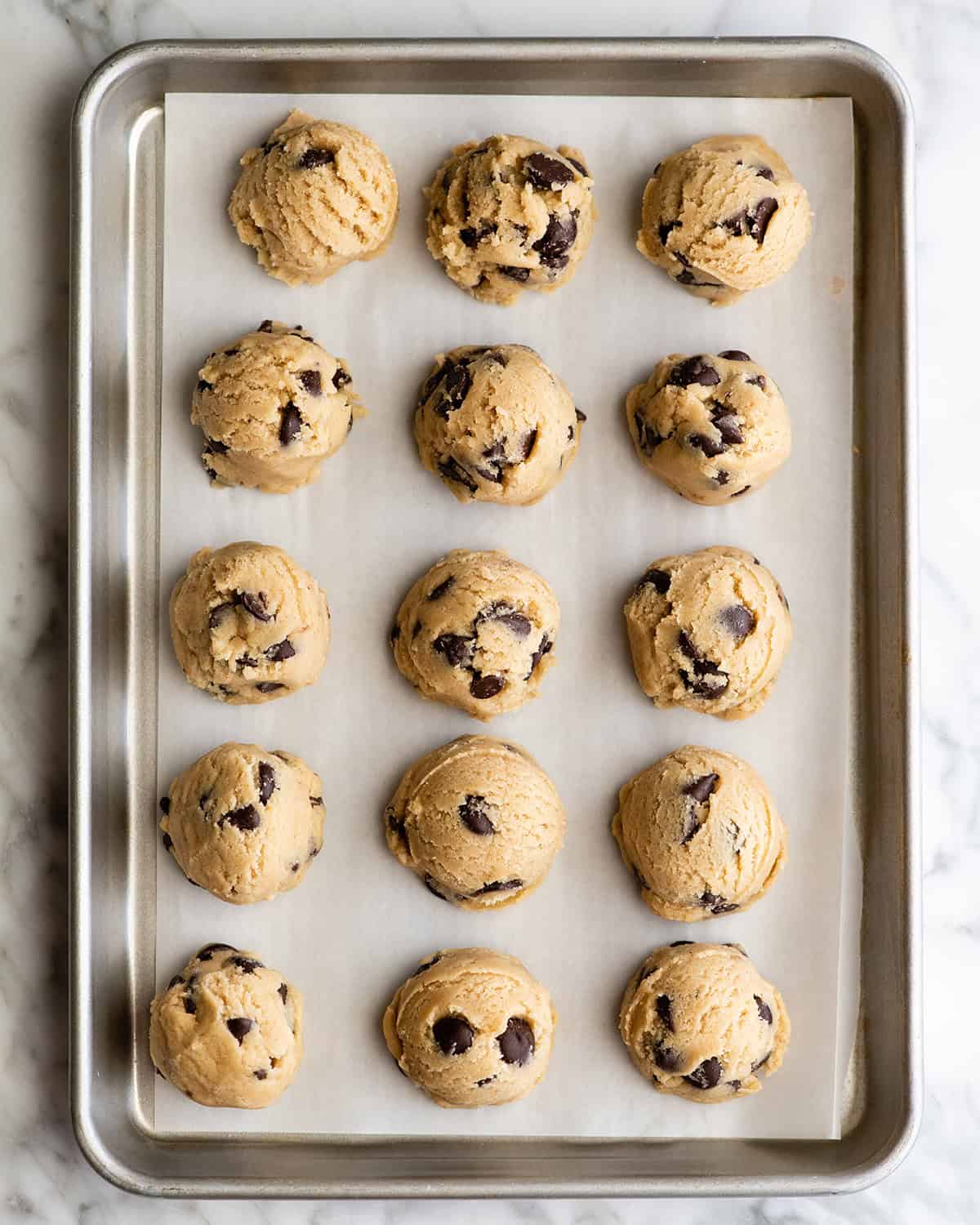 how to make chocolate chip cookies - 15 cookie dough balls on a parchment paper lined baking sheet to flash freeze.