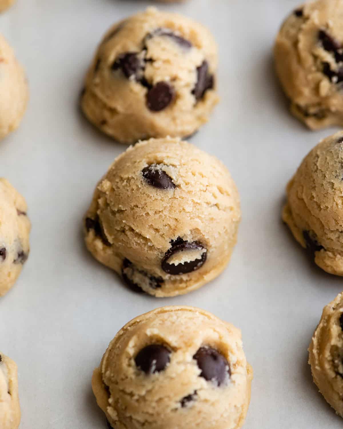how to make chocolate chip cookies - close up photo of 9 cookie dough balls on a parchment paper lined baking sheet to flash freeze so the texture is visible.