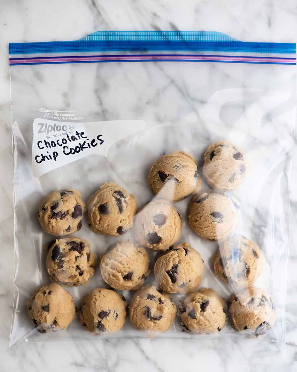 how to freeze chocolate chip cookies - 15 cookie dough balls in a clear plastic bag labeled "chocolate chip cookies" on a marble surface to be frozen