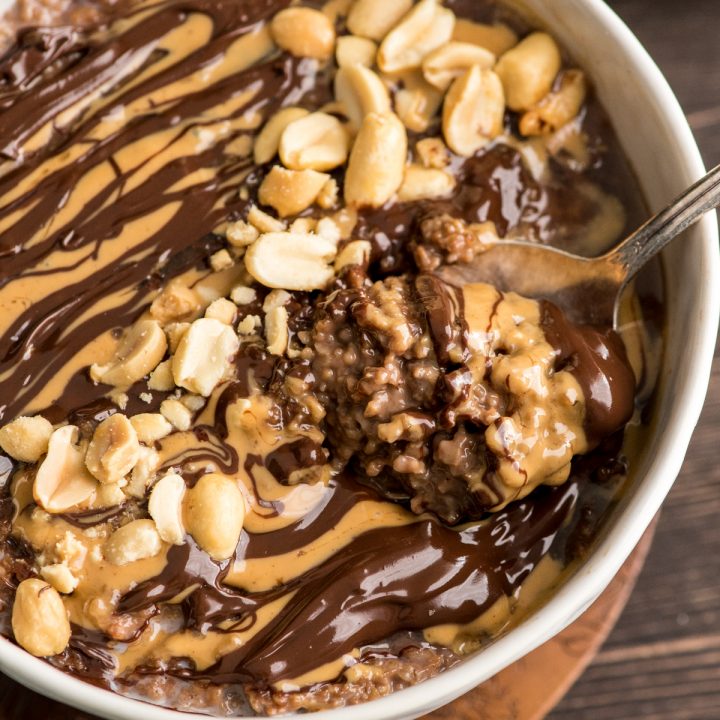 Overhead view of a bowl of chocolate peanut butter oat bran with swirls of peanut butter and chocolate and crushed peanuts with a spoon in it 