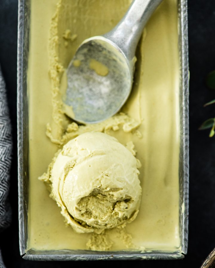 overhead view of a rectangular metal container filled with dairy-free matcha ice cream with a scoop formed and an ice cream scoop 
