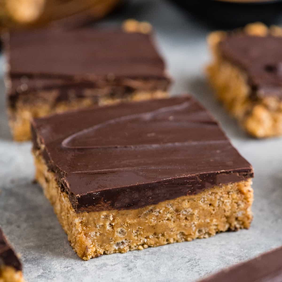 Close up side view of a healthy peanut butter rice crispy treat cut into a square with two more in the background. 