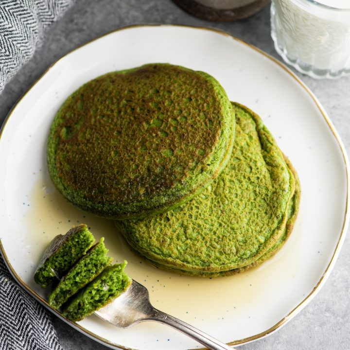 two spinach pancakes on a plate with maple syrup