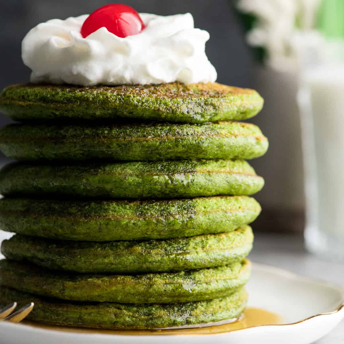 Front view of a stack of 7 spinach oatmeal pancakes topped with whipped cream and a cherry