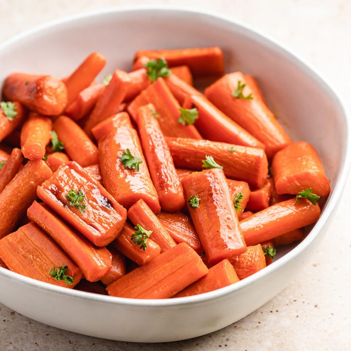 a white bowl of Honey Roasted Carrots garnished with carrot greens