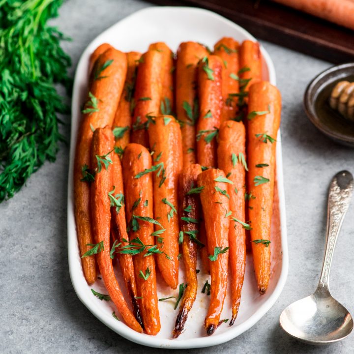 honey roasted carrots on a white serving dish garnished with carrot greens. 