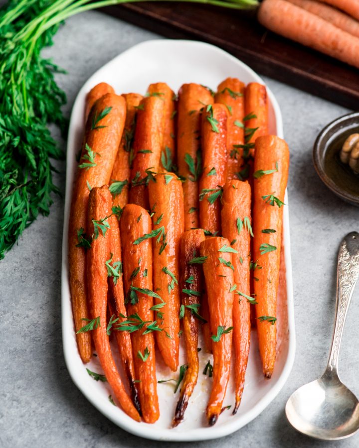 honey roasted carrots on an oval platter sprinkled with carrot greens