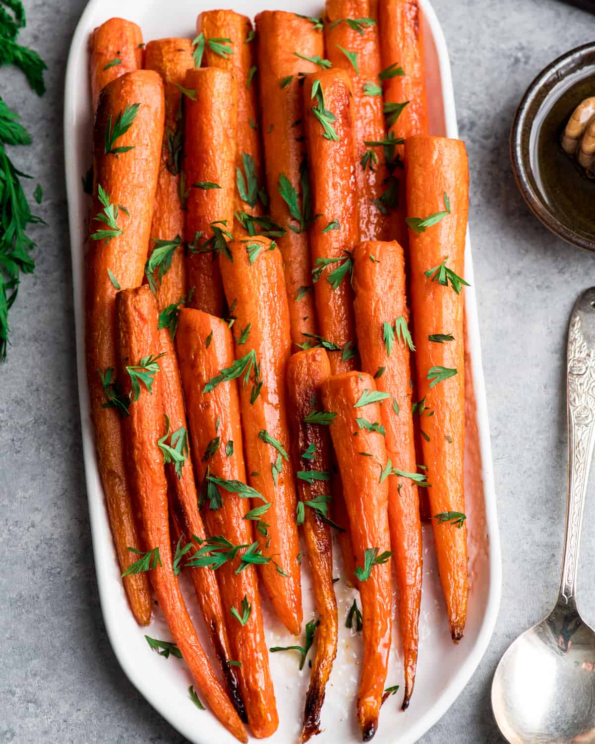 Overhead view of honey roasted carrots on an oval platter sprinkled with carrot greens
