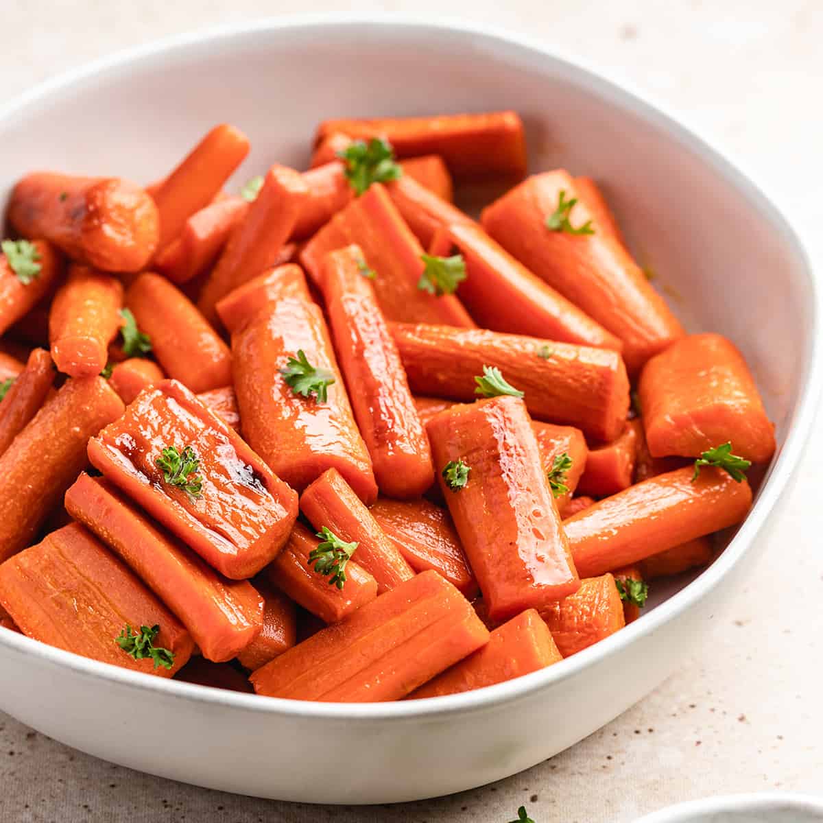 honey glazed carrots in a white bowl garnished with carrot greens