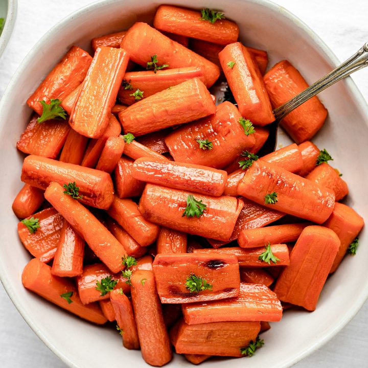 Honey Roasted Carrots in a white bowl garnished with carrot greens