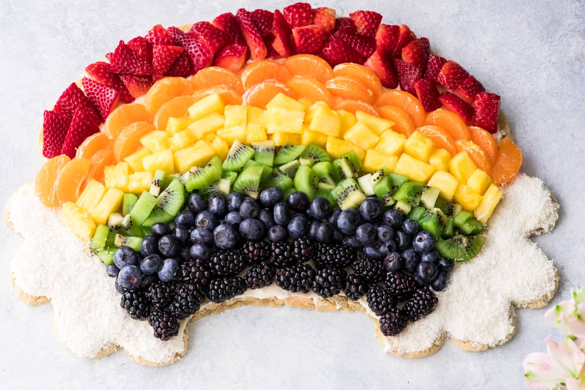 overhead view of a rainbow fruit pizza recipe in the shape of a rainbow with coconut clouds