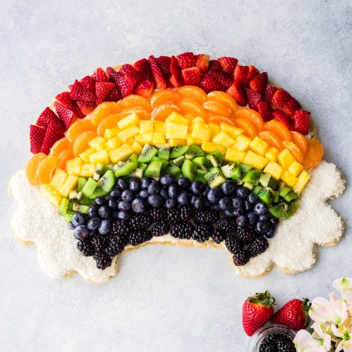 overhead view of a rainbow fruit pizza recipe in the shape of a rainbow with coconut clouds
