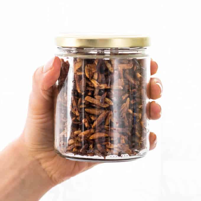Front view of easy candied almonds in a glass jar with a gold top being held in a hand 