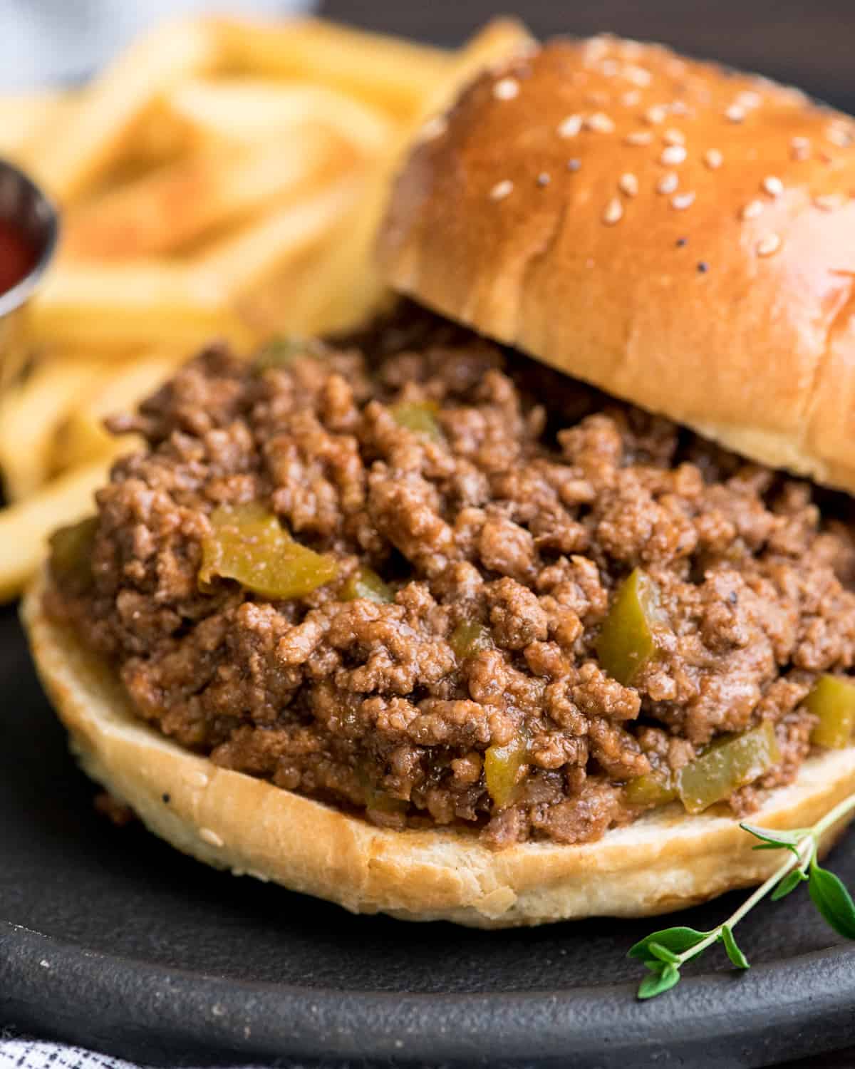 Up close front shot of healthy sloppy joes recipe on a bun with the top of the bun off to the side and french fries in the background