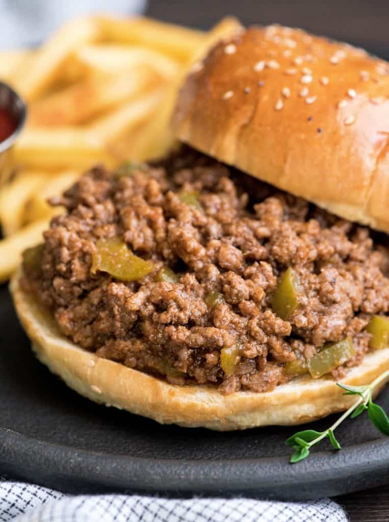 van dichtbij schot van het recept van gezonde sloppy joes op een broodje met de bovenkant van het broodje aan de zijkant en frietjes op de achtergrond