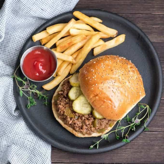 Overhead view of healthy sloppy joes recipe on a bun with pickles on a round black plate with ketsup and french fries and fresh thyme