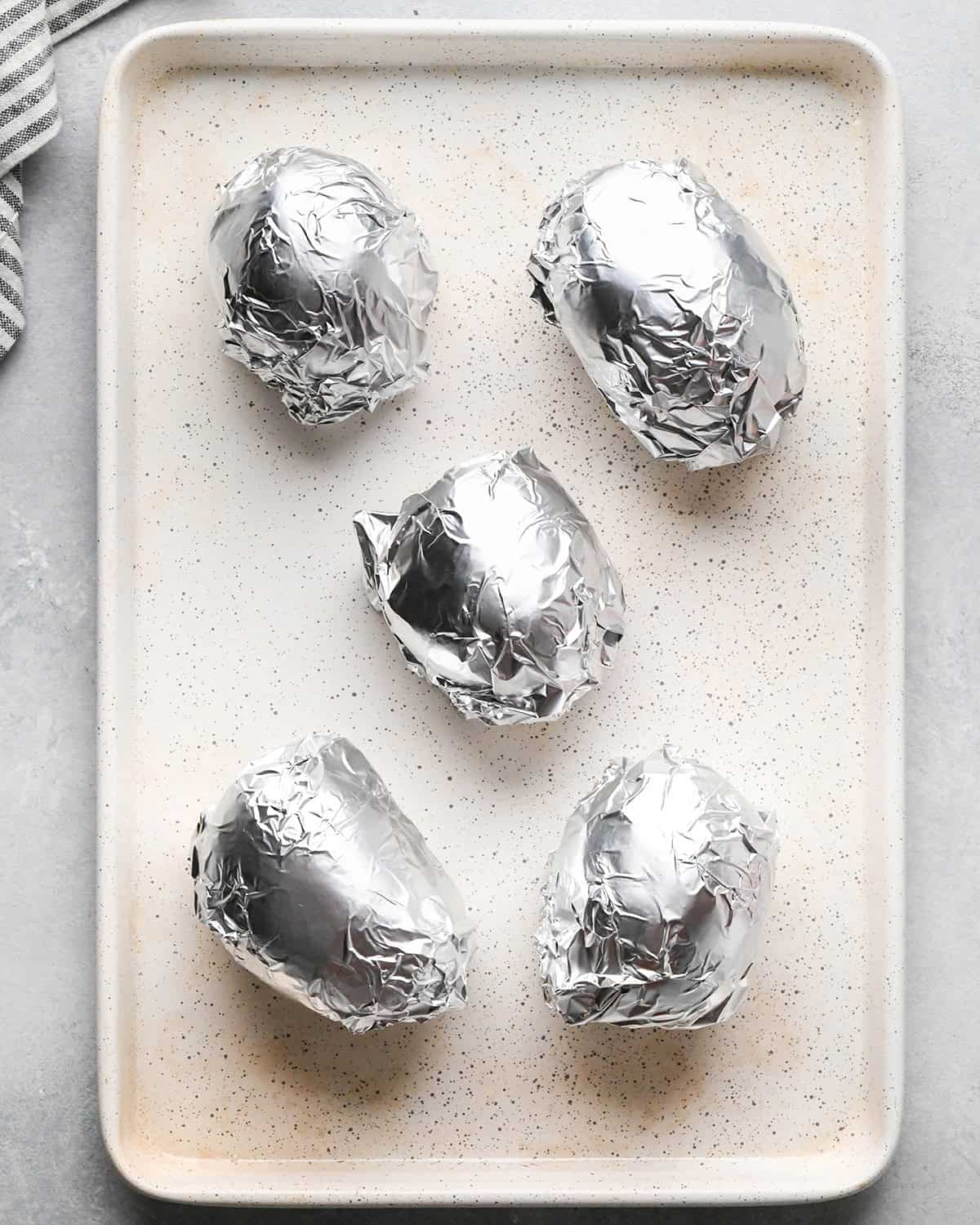 5 potatoes wrapped in foil on a baking sheet