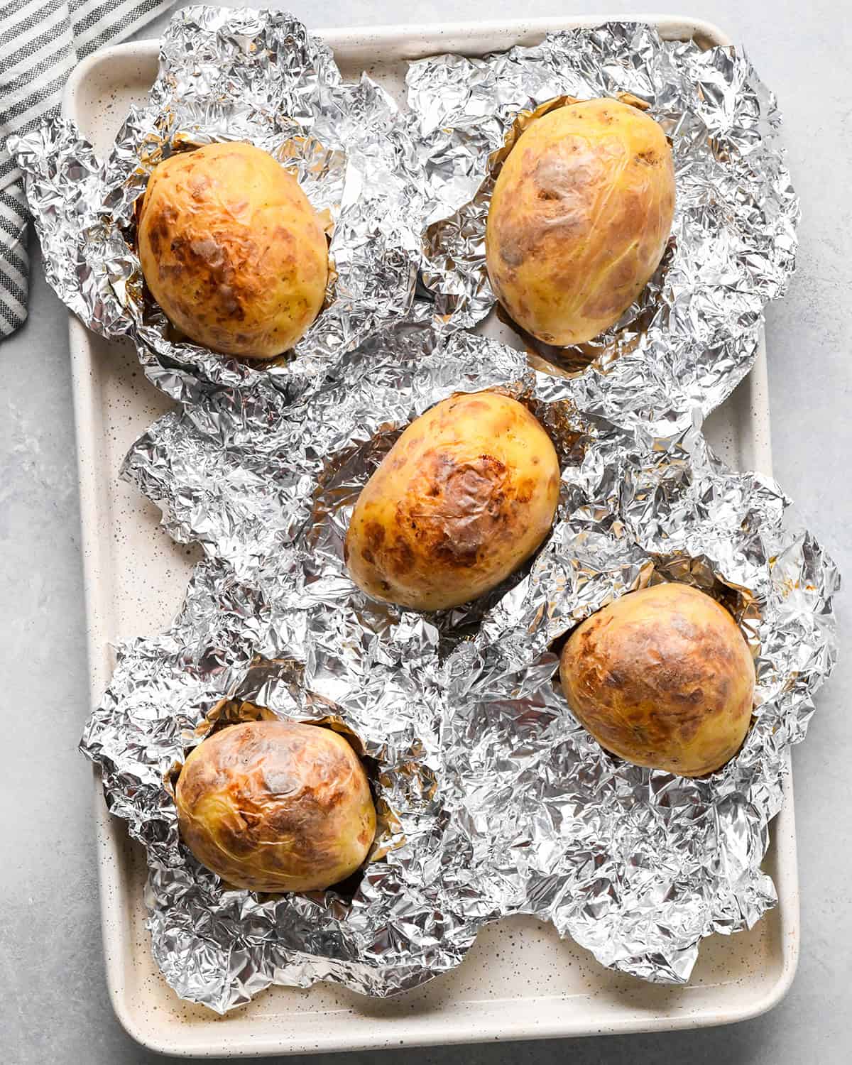 5 baked potatoes unwrapped from foil on a baking sheet