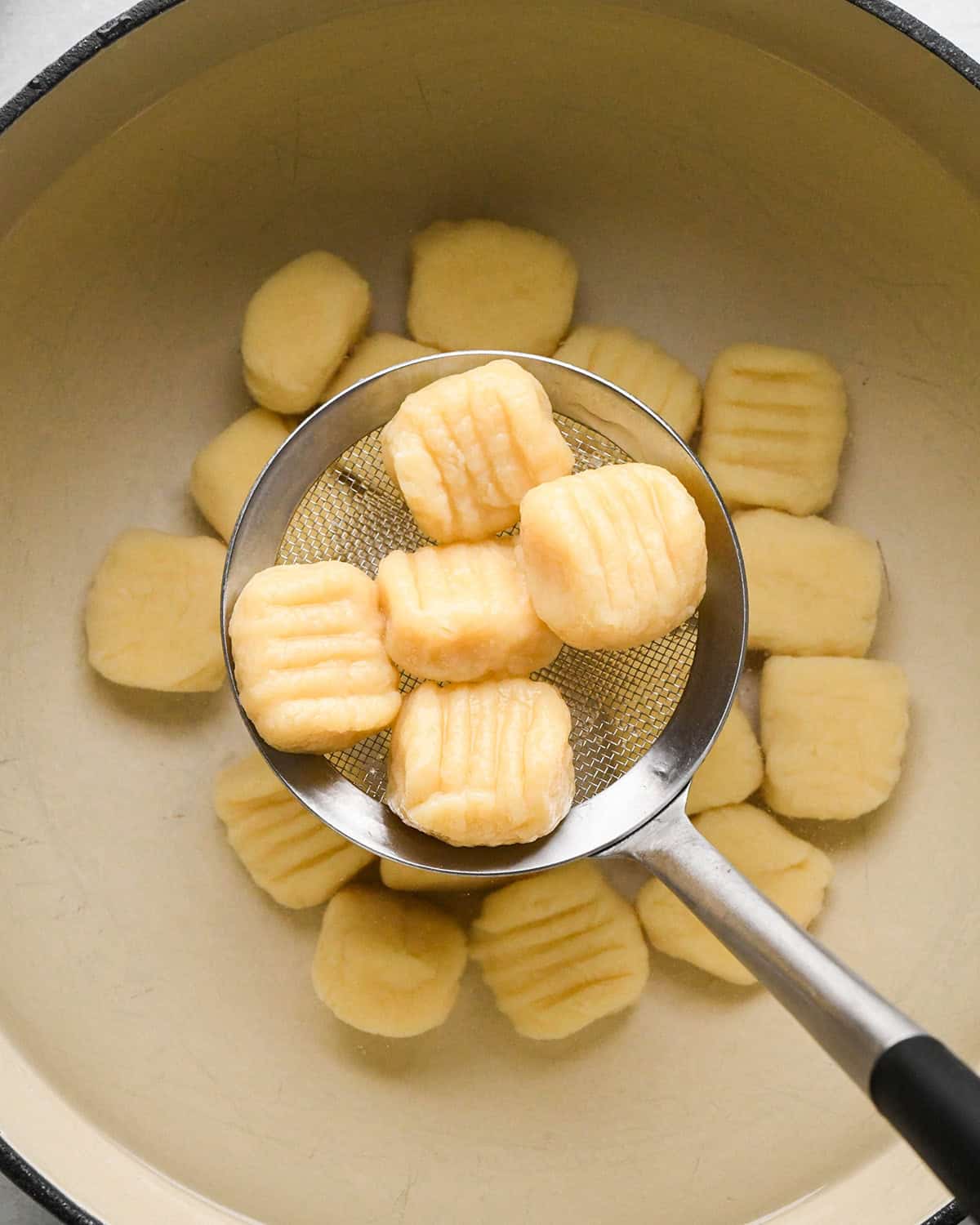 potato gnocchi being removed from boiling water with a spoon