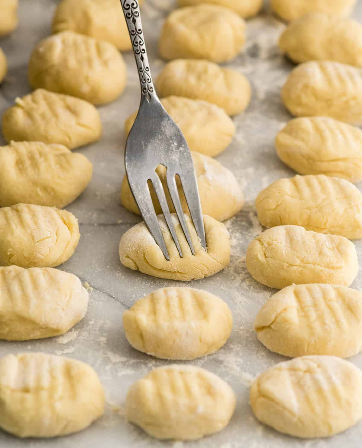 Front view of three rows of Homemade Potato Gnocchi and the gnocchi in the middle of the frame is being indented with a floured fork 