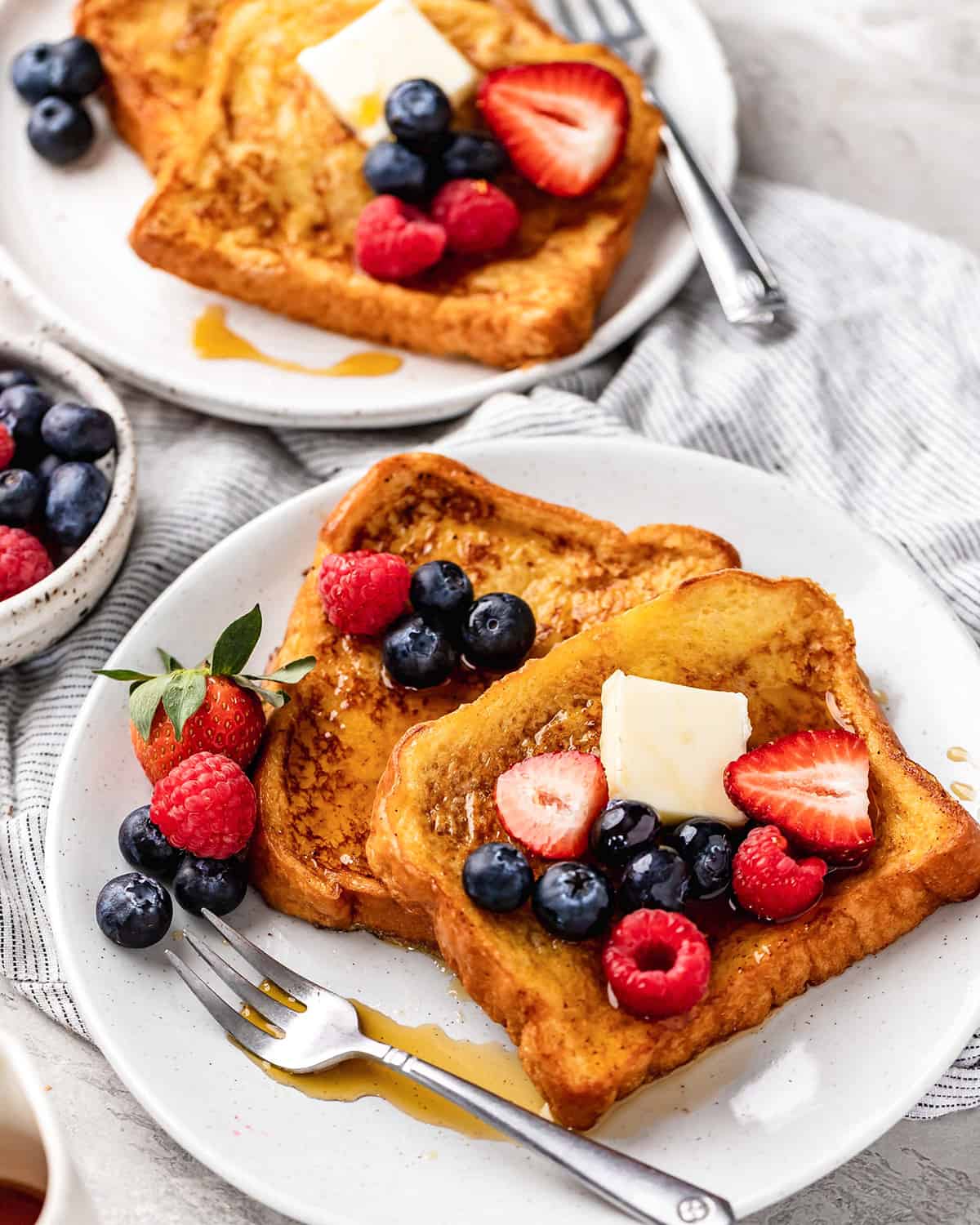 two pieces of french toast on a plate with butter, syrup and berries