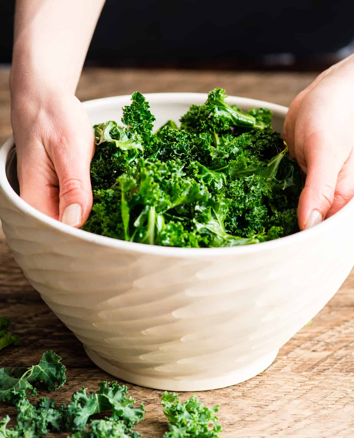Hands in a bowl massaging olive oil into kale leaves showing how to make kale chips