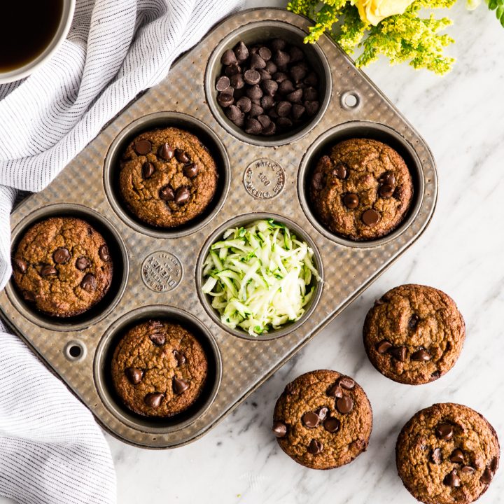 Overhead view of a muffin tin with baked Paleo Zucchini Banana Muffins in it and three outside of it