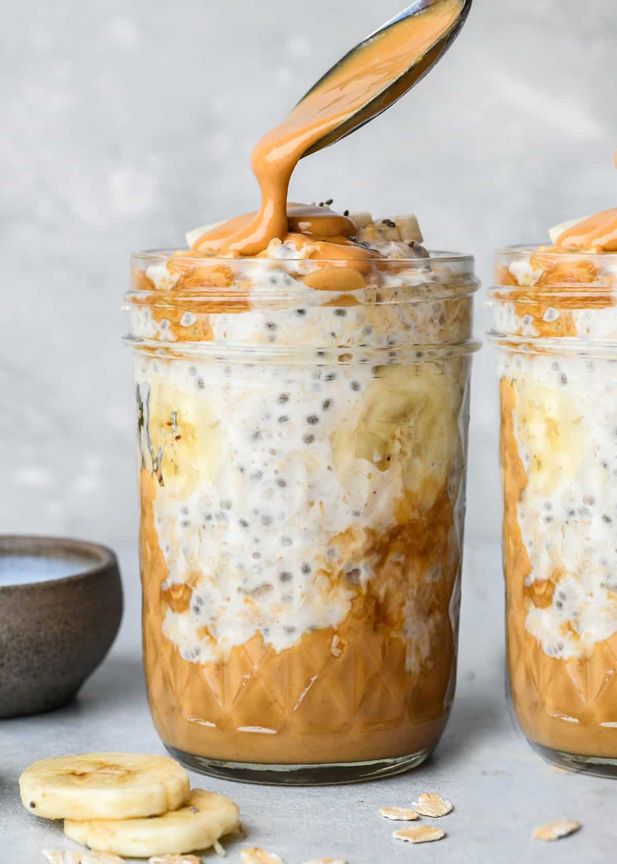 a spoon putting peanut butter on top of a jar of Peanut Butter Overnight Oats