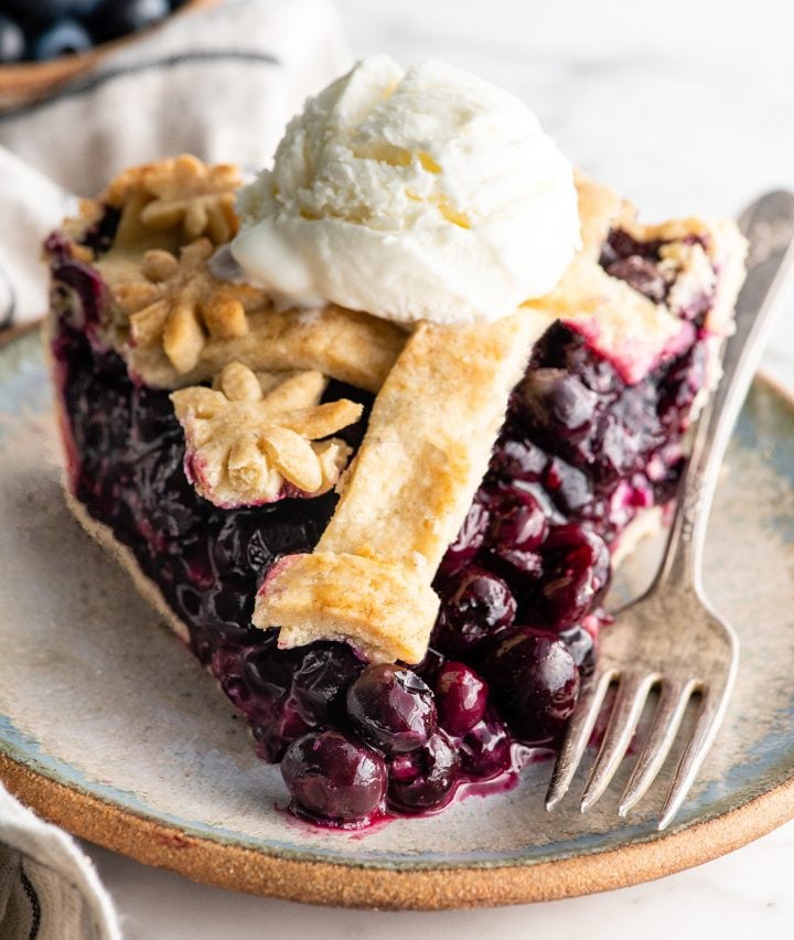 front view of a slice of blueberry pie with a scoop of ice cream on top