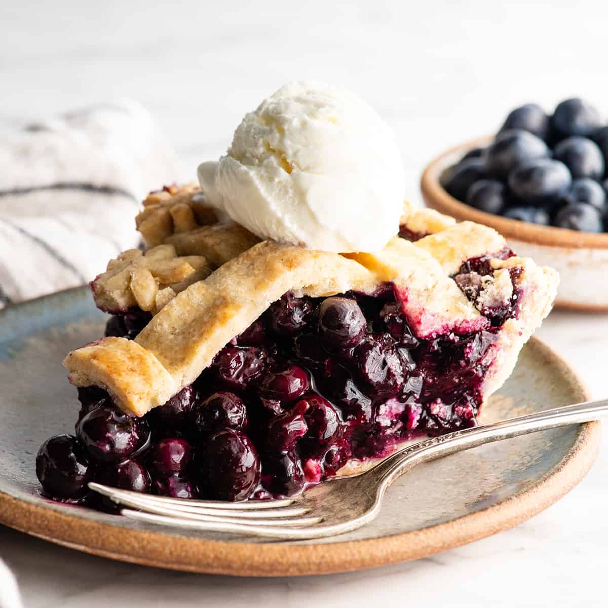 front view of a slice of blueberry pie with a scoop of vanilla ice cream on top