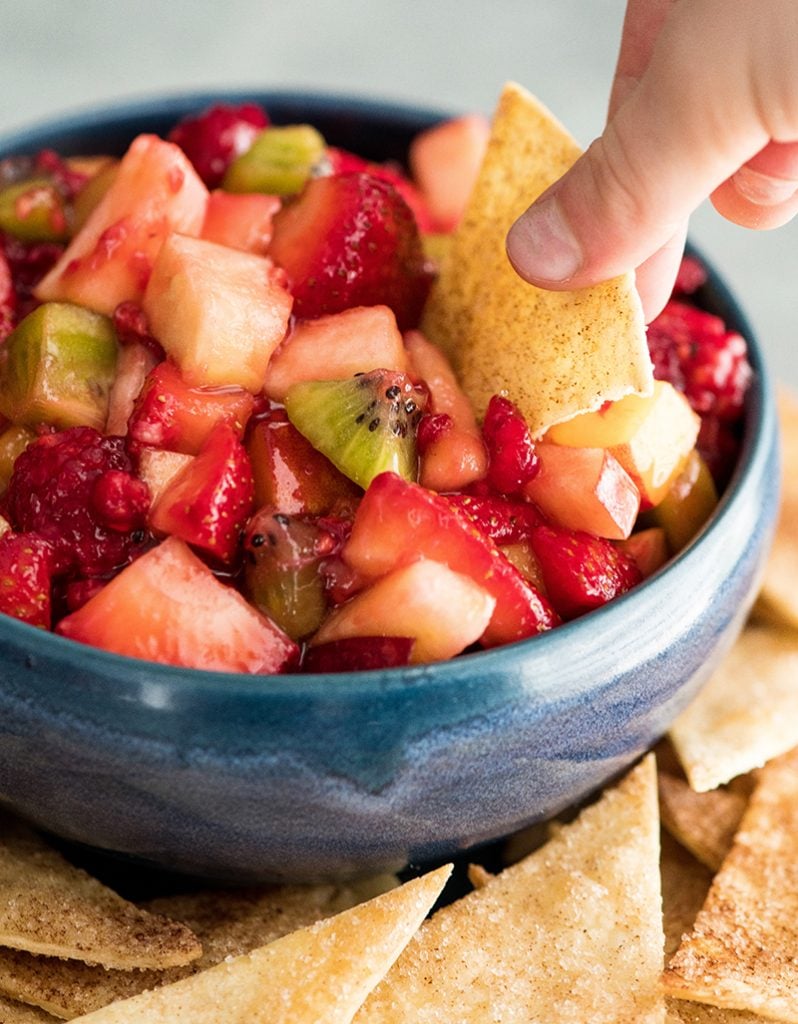 Up close, front view of a hand dipping a cinnamon chip into a bowl of fruit salsa