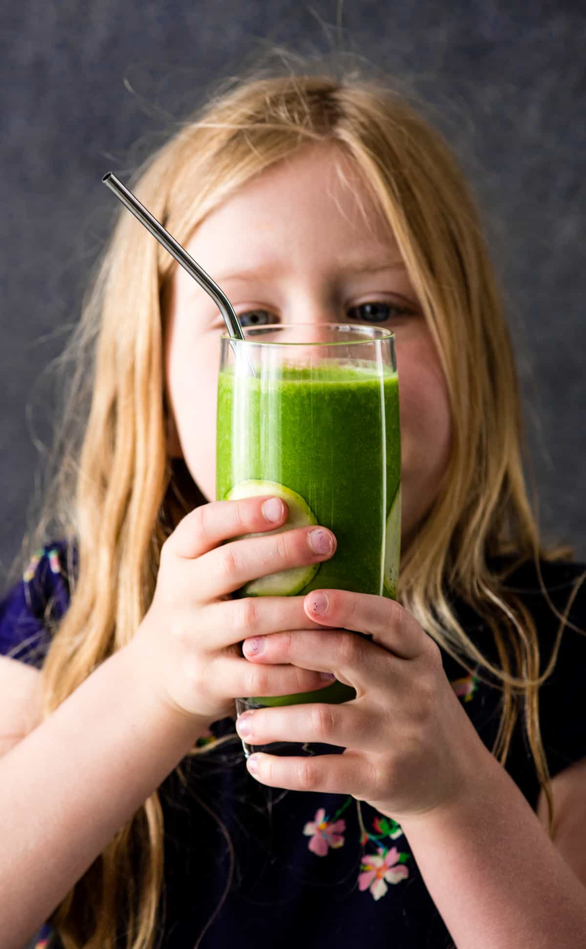 Front view of a little girl holding a Zucchini Smoothie looking at it