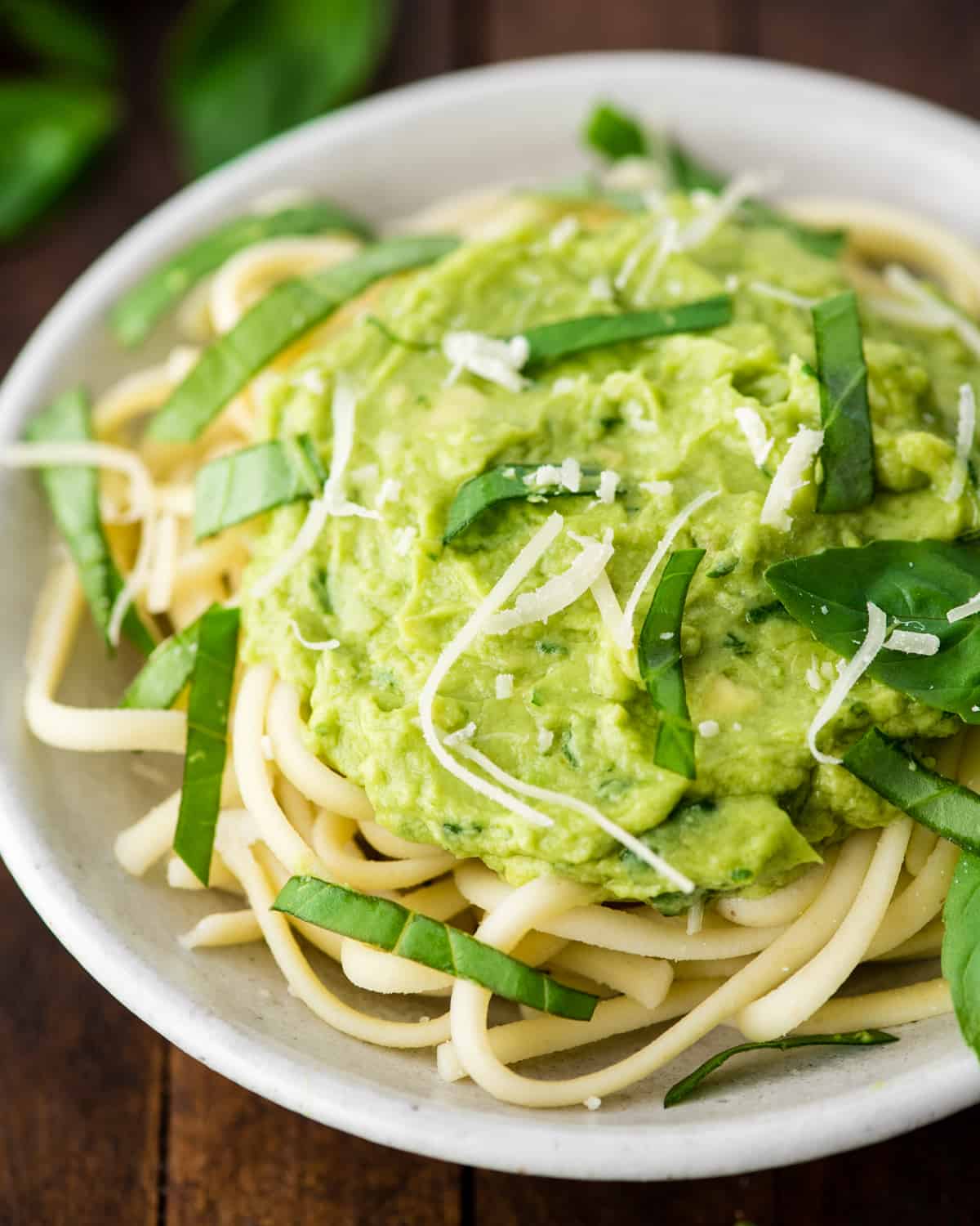front view of a bowl of pasta with Avocado Pasta Sauce on top garnished with fresh basil and parmesan cheese