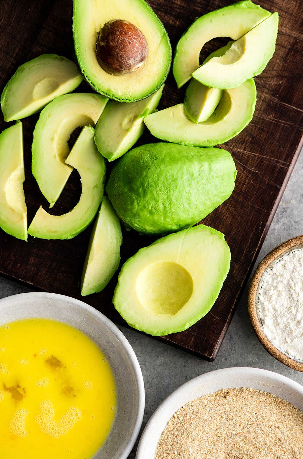 Overhead visning af avocados på et skærebræt både skåret op og skrællet i fremstillingen af denne bagt Avocado Fries Opskrift