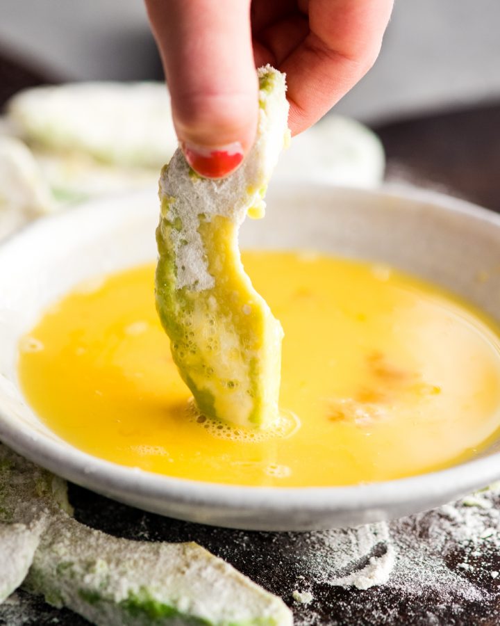 photo showing How to Make Avocado Fries - dipping the floured avocado slice in egg 