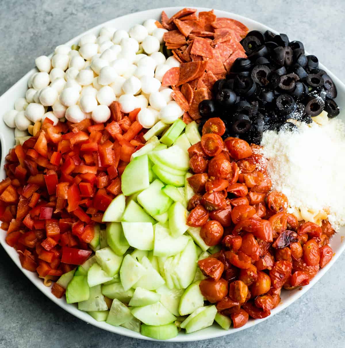 overhead view of the best pasta salad recipe in a large white serving bowl with all the ingredients organized separately before being mixed together