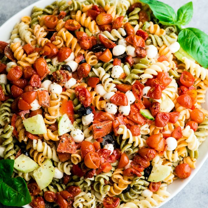 overhead view of the best pasta salad recipe in a large white serving bowl with a wooden spoon taking a scoop