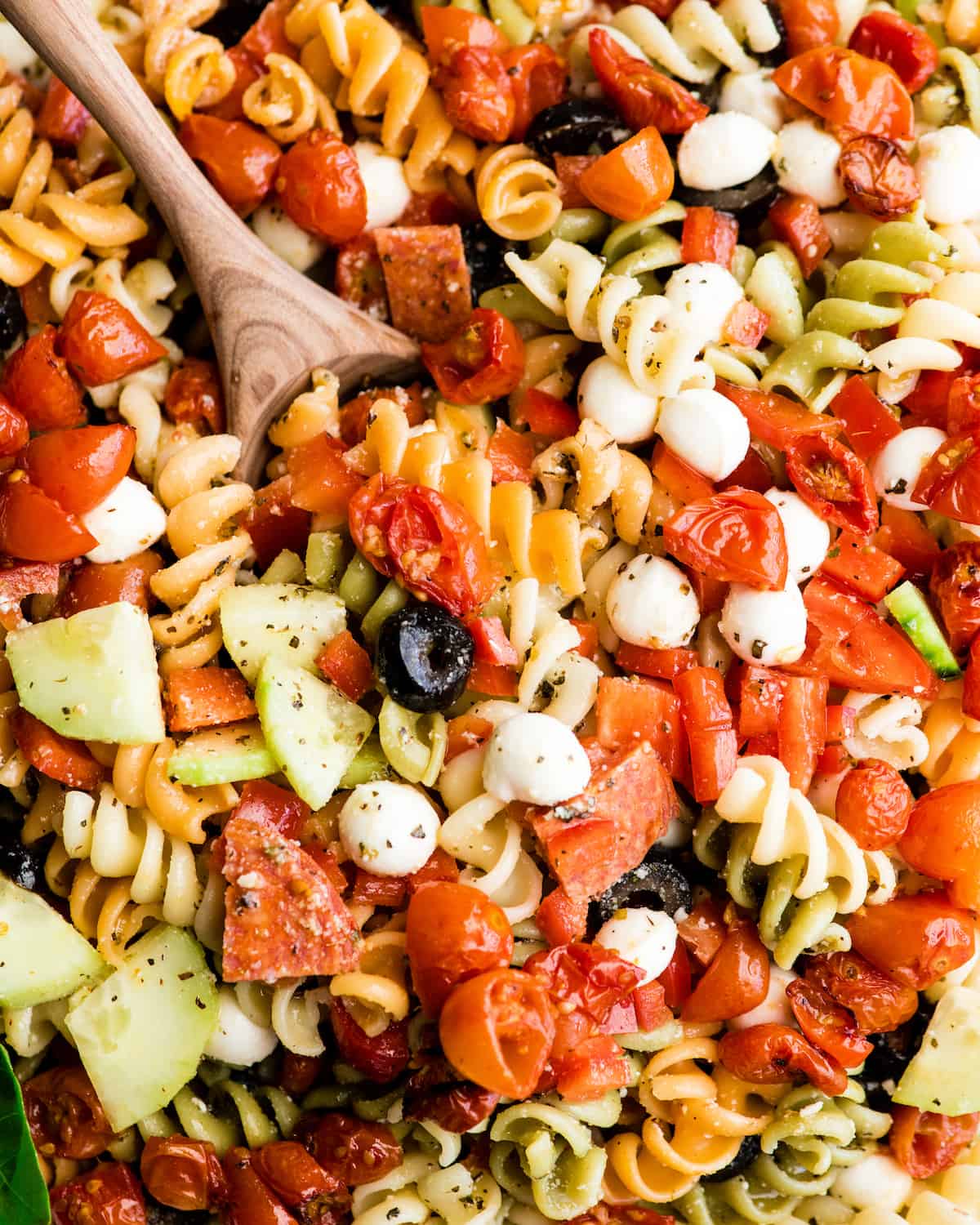 overhead view of the best pasta salad recipe in a large white serving bowl with a wooden spoon taking a scoop