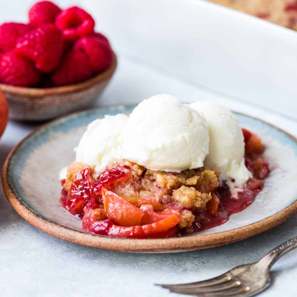 front view of a serving of Raspberry Peach Crisp on a plate topped with vanilla ice cream