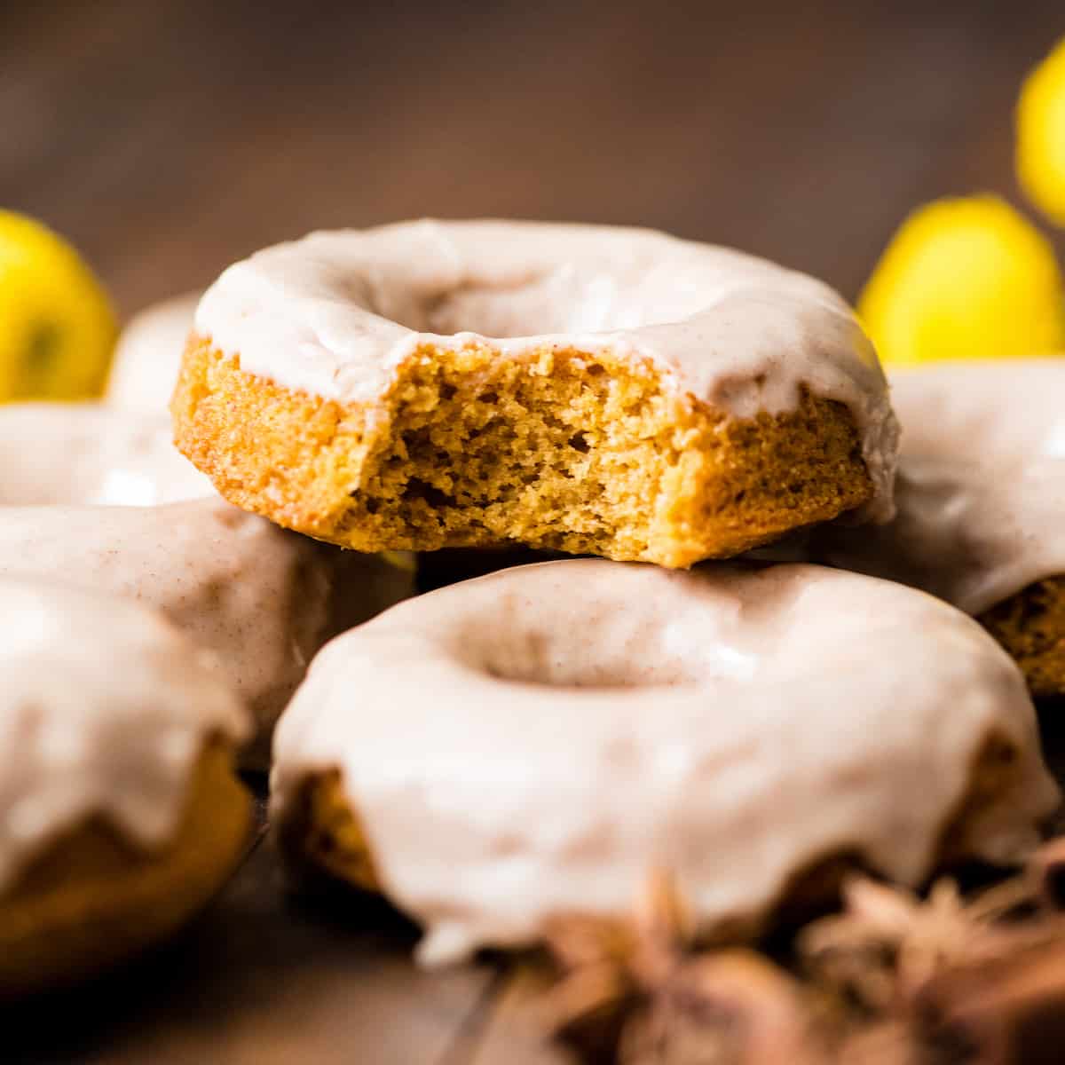Front view of a Baked Pumpkin Donut with a bite taken out of it stacked on five other pumpkin donuts. 