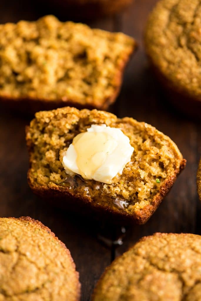 up close front/overhead view of a Carrot Zucchini Muffin cut in half with a pat of butter and a drizzle of honey