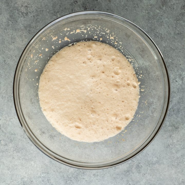 overhead photo showing yeast proofing in a glass bowl to make homemade pizza dough