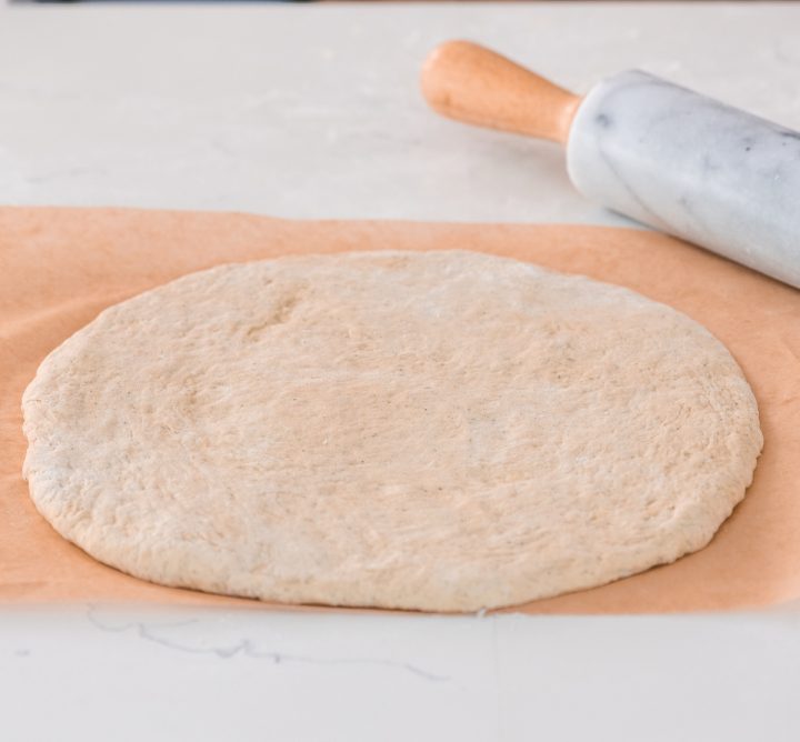 front view showing How to Make Pizza Dough - dough rolled out on parchment paper
