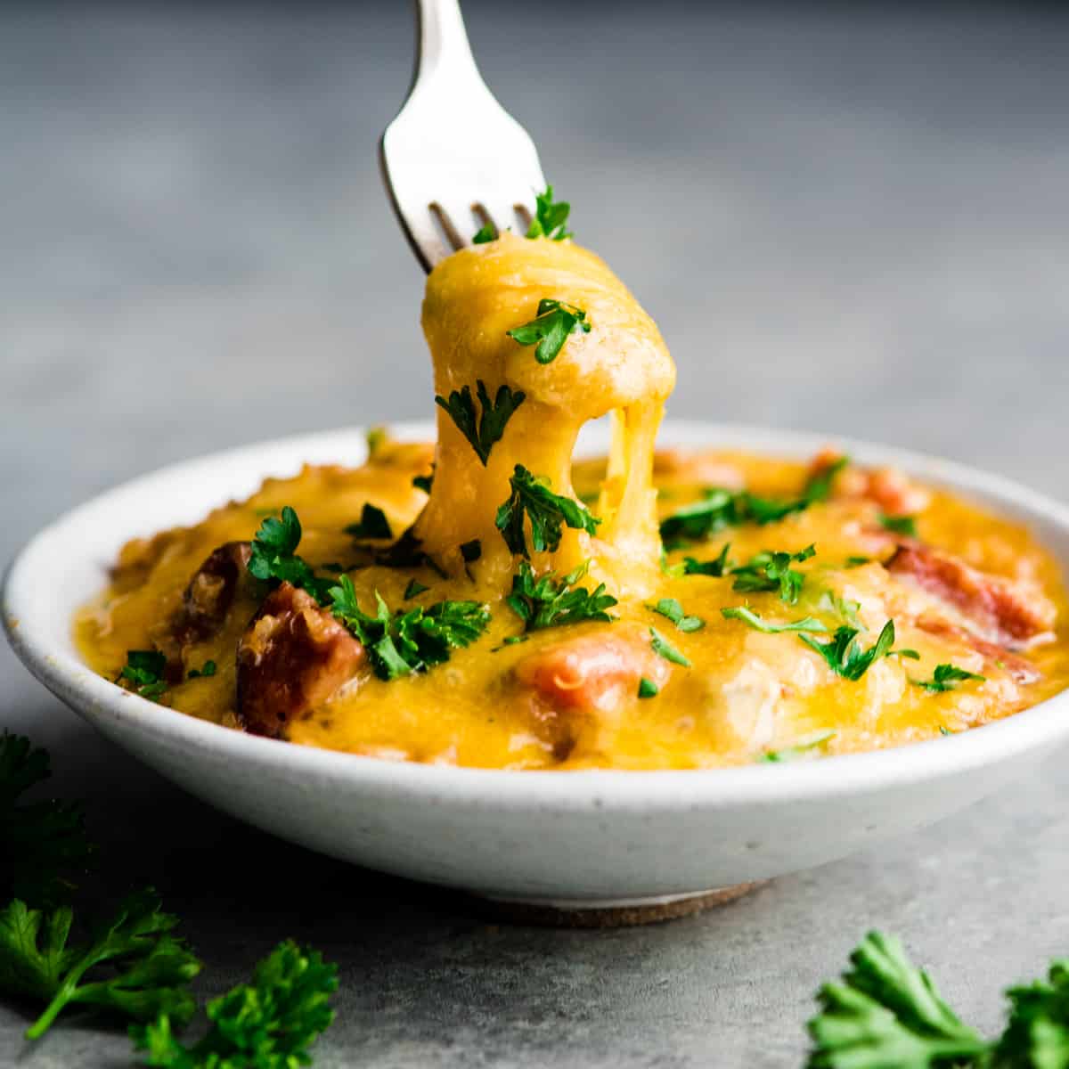 front view of a fork lifting a bite of Baked Quinoa Casserole out of a bowl showing a stringy cheese pull topped with fresh parsley