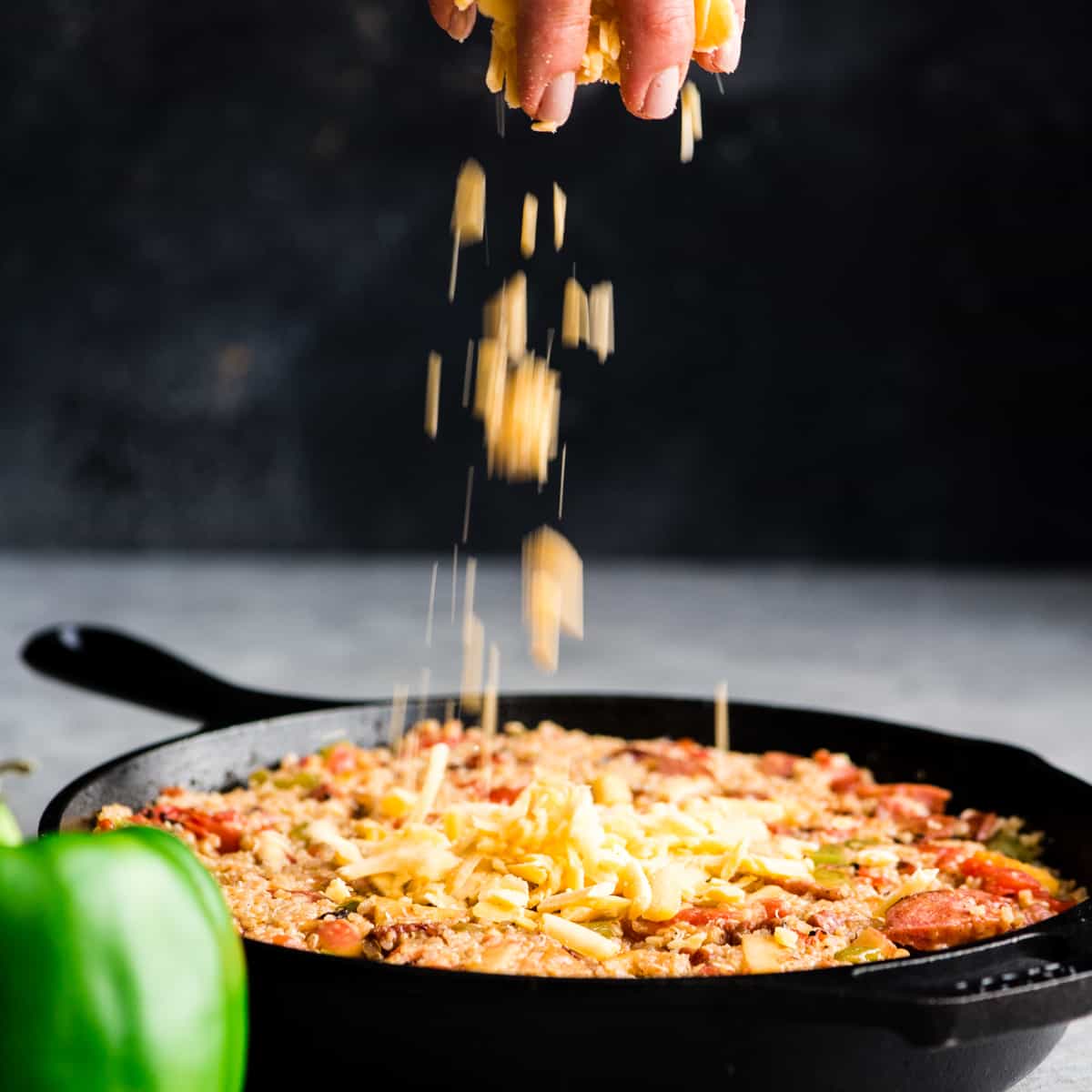 front view of a hand sprinkling shredded cheddar cheese on top of a skillet full of Baked Quinoa Casserole 