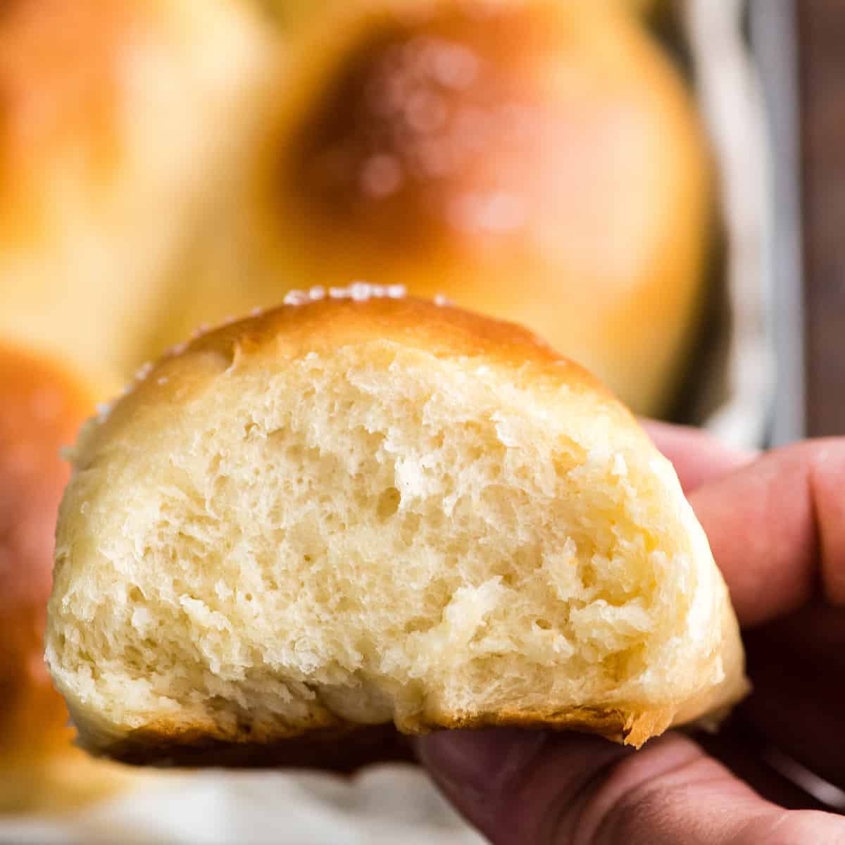 front view of a hand removing one Best Homemade Dinner Rolls from the pan 