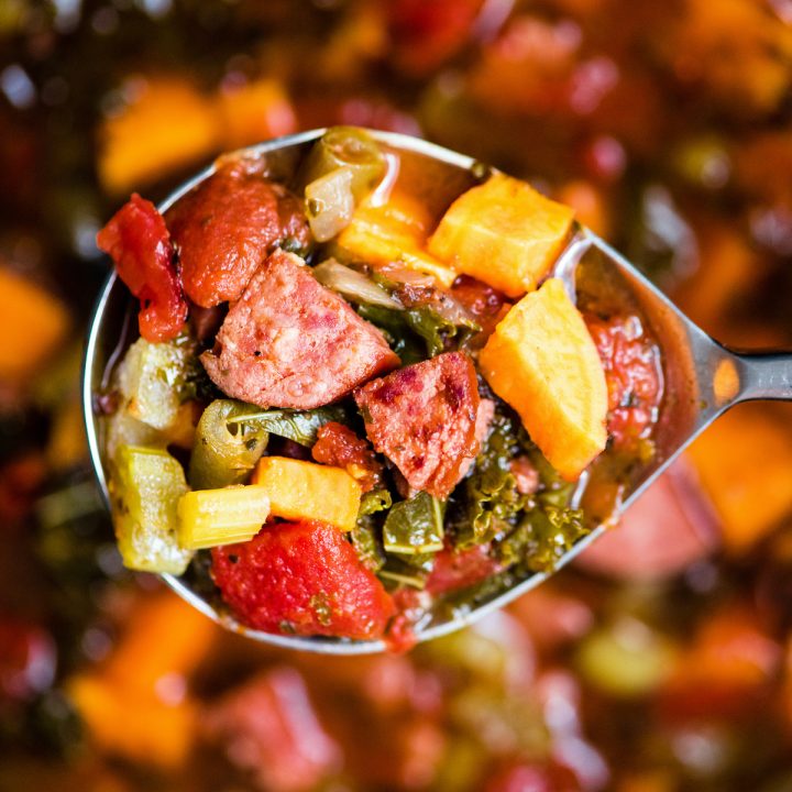 up close overhead view of a spoon with a scoop of Sausage Kale Soup on it hovering over the crock pot where the rest of the Sausage Kale Soup is