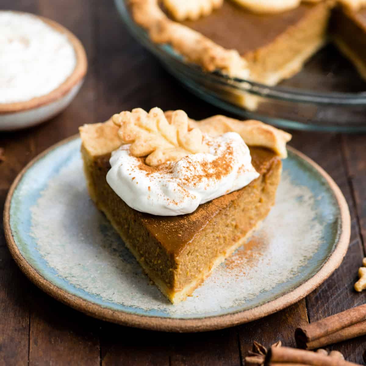 front view of a slice of dairy-free pumpkin pie on a plate with a dollop of whipped cream