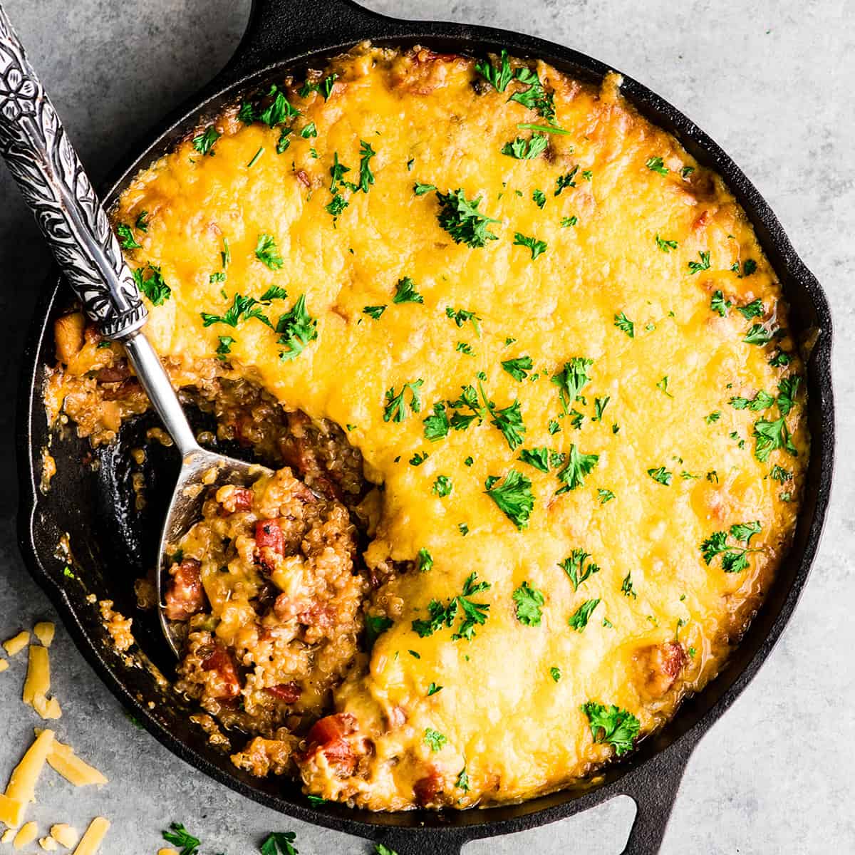 overhead view of baked quinoa casserole in a cast iron pan with a spoon taking a scoop out of it